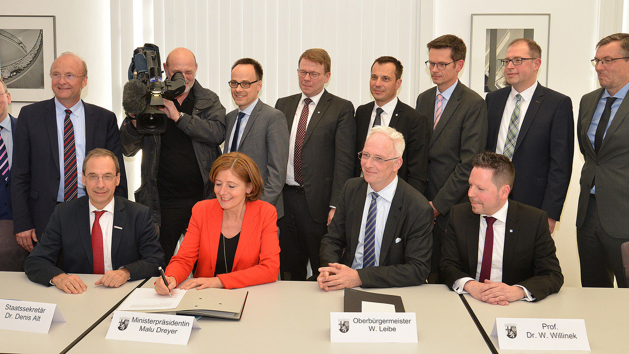 (hintere Reihe, v.l.) Dr. Günther Mattheis, Präsident der Landesärztekammer Rhld.-Pf., Prof. Dr. Ulrich Förstermann (Wissenschaftlicher Vorstand und Dekan Universitätsmedizin Mainz), Dr. Denis Alt, Staatssekretär Wissenschaftsministerium,  Prof. Norbert Pfeiffer, Medizinischer Vorstand Universitätsmedizin Mainz; Dr. Wolfgang Thomas, Ärztlicher Direktor am Klinikum Mutterhaus der Borromäerinnen (sitzend, v. l.) Prof. Winfried Willinek, Ärztlicher Direktor Krankenhaus der Barmherzigen Brüder; Ministerpräsidentin Malu Dreyer,  Trierer Oberbürgermeister Wolfram Leibe; Prof. Dr. med. Winfried A. Willinek, Ärztlicher Direktor Krankenhaus der Barmherzigen Brüder Trier) und weitere Vertreter der Kooperationspartner bei der Unterzeichnung.