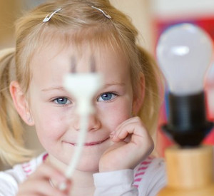 Eine Glühlampe mit einem Kind im Hintergrund, das den Stecker der Lampe in der Hand hält; Bild: dpa