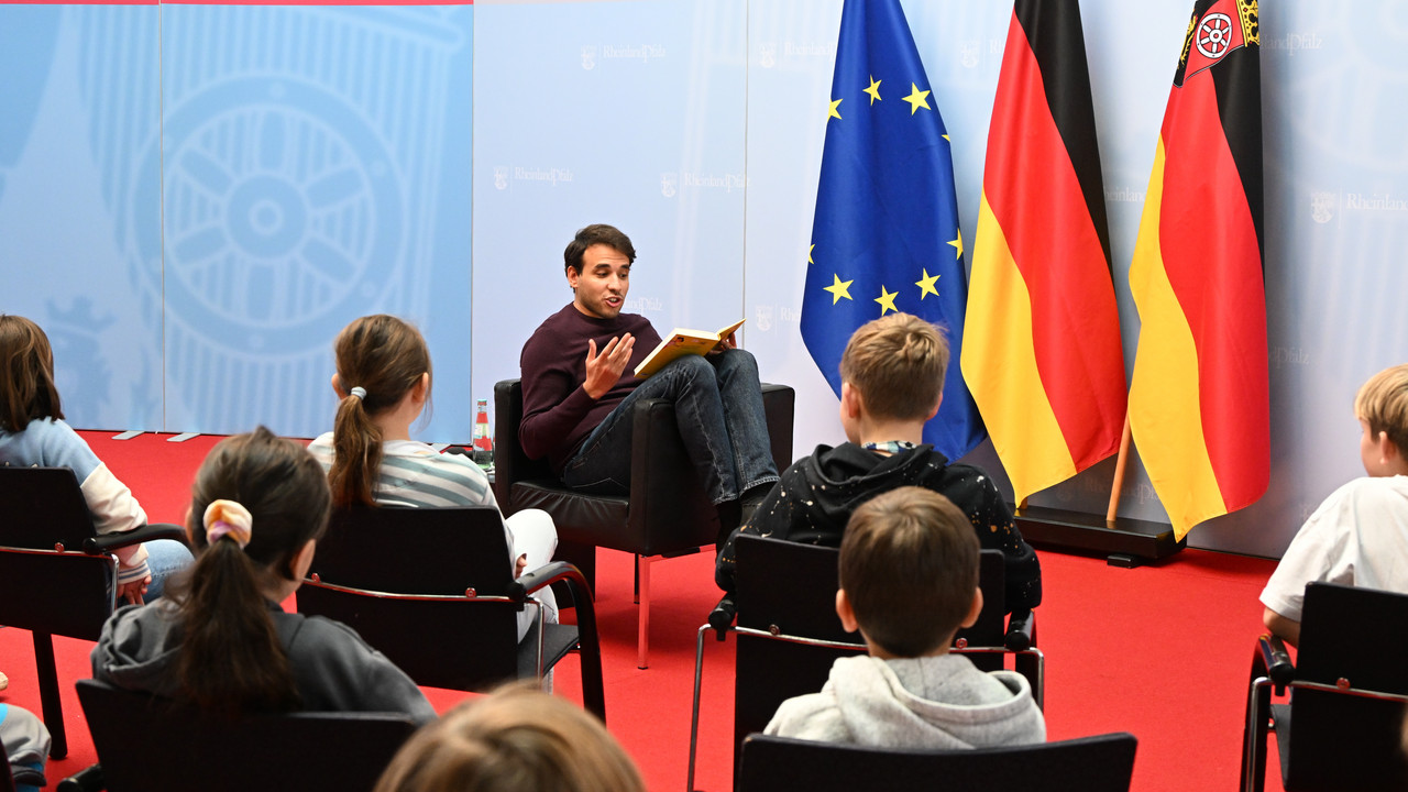 TV-Moderator und Lesebotschafter Sherif Rizkallah einer 5. Klasse der IGS Nieder-Olm aus dem Buch „Ada und die Künstliche Blödheit: Ein Roboter auf der Flucht“ von Franziska Gehm vor. 