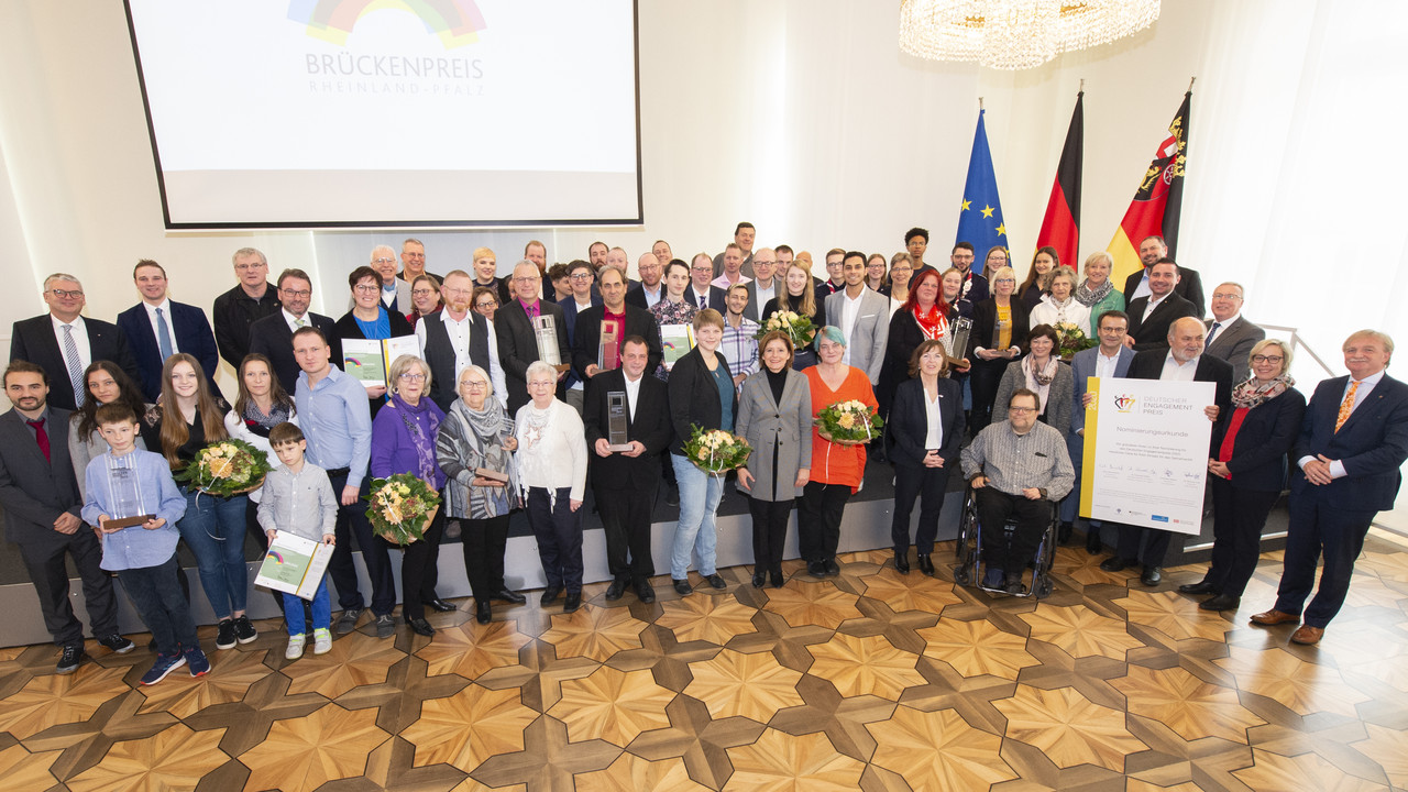 Gruppenfoto der Ministerpräsidentin mit allen Preisträgerinnen und Preisträgern des Brückenpreises 2019 auf und vor der Bühne im Festssaal der Staatskanzlei.