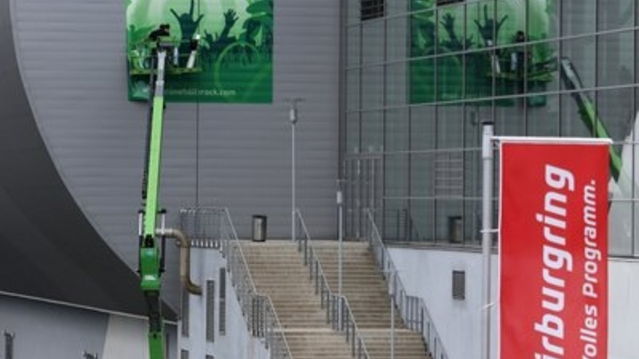 Arbeiter kleben am Nürburgring in Nürburg  ein Plakat für die Veranstaltung "Grüne Hölle"-Rockfestival an das Gebäude der Ring-Arena. Bild: dpa