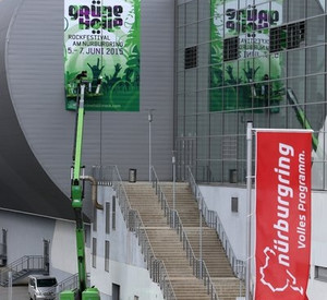 Arbeiter kleben am Nürburgring in Nürburg  ein Plakat für die Veranstaltung "Grüne Hölle"-Rockfestival an das Gebäude der Ring-Arena. Bild: dpa