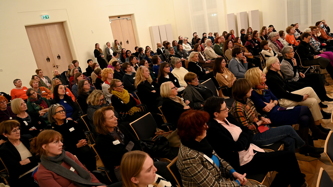 Frauen jeden Alters sitzen im Publikum und hören den Sprecherinnen auf dem Podium zu.