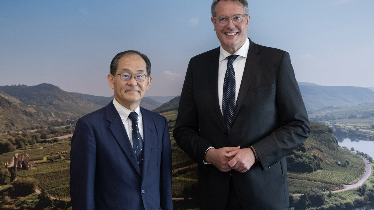 Der japanischen Botschafter Hidenao Yanagi steht neben Ministerpräsident Alexander Schweitzer. Im Hintergrund ein Wandbild der Moselschleife.