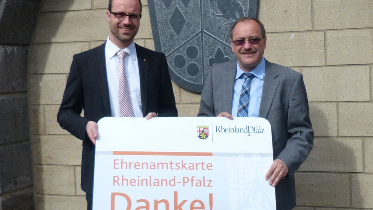 Der Chef der Staatskanzlei, Staatssekretär Clemens Hoch, und Verbandsbürgermeister Gerd Heilmann halten eine Ehrenamtskarte in großem Format; Bild: VG Vordereifel
