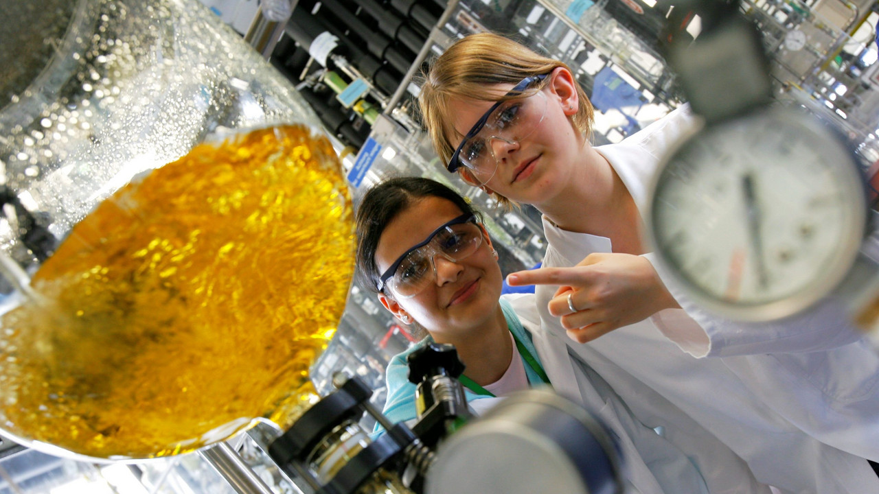 Zwei Schülerinnen betrachten, wie Wasser mit einem Farbstoff in einem Glaskolben gemischt wird.