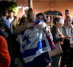 Demonstrantin umarmt andere Demonstrantin, welche Israelflagge über den Rücken gehängt trägt.